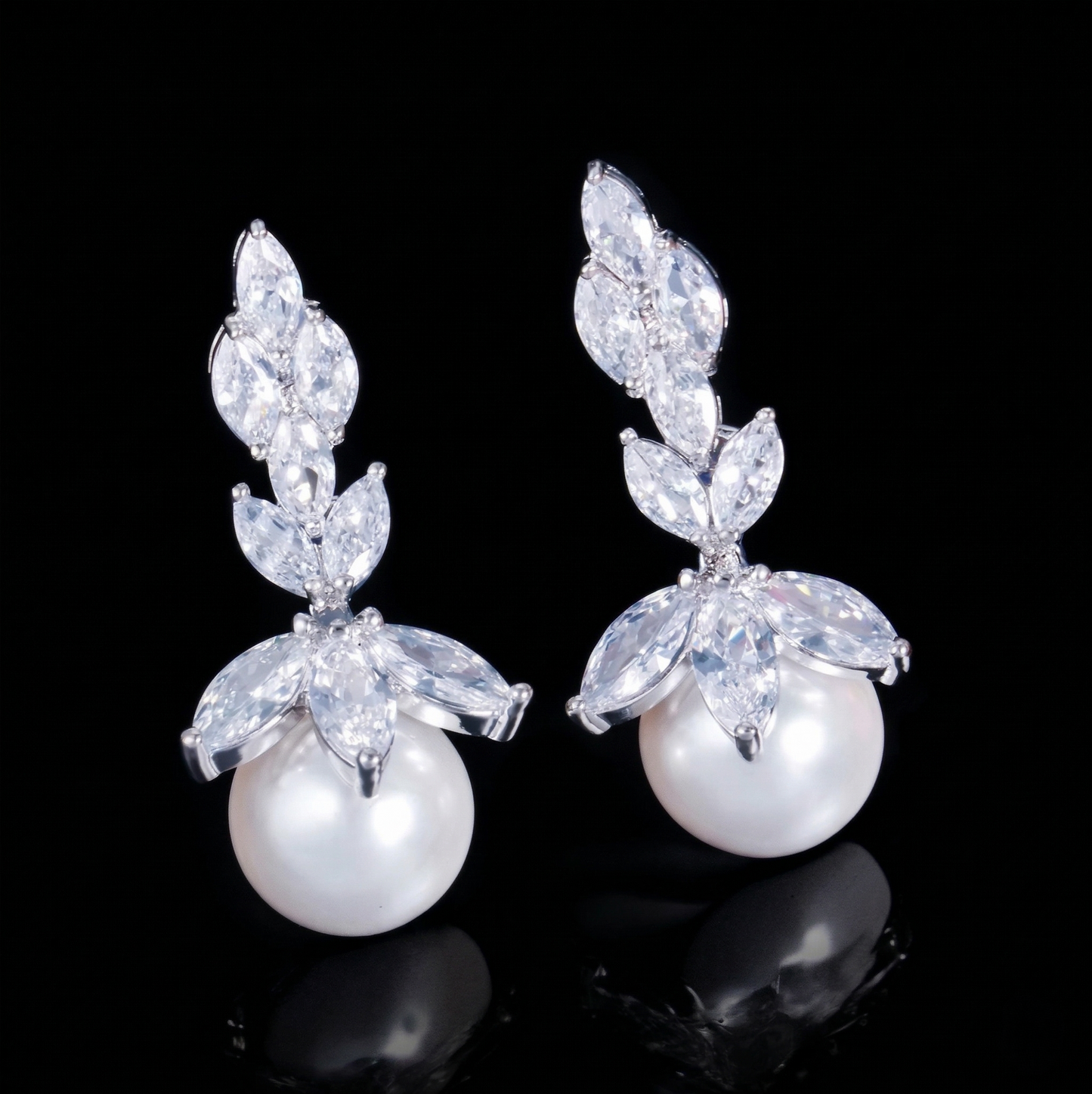 Pair of elegant drop earrings featuring shimmering marquise-cut cubic zirconia arranged in a botanical leaf silhouette with a round white faux pearl hanging at the bottom, isolated on a reflective black background.