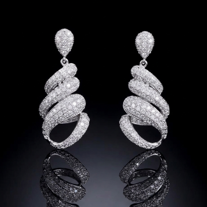 Luxurious silver-tone spiral earrings featuring dense pavé stone setting, captured against a pitch-black background with a crisp reflection on a glossy surface, highlighting high-end craftsmanship.