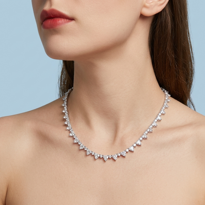 High-end jewelry campaign photograph featuring a female model wearing a sophisticated crystal heart-design necklace, set against a solid, uniform light blue background.