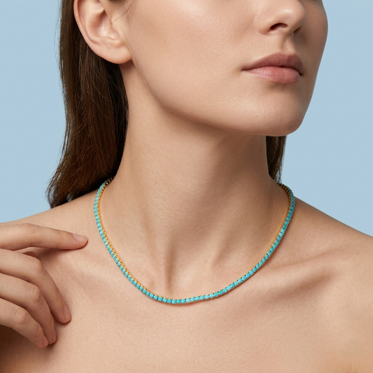 Detailed shot of a woman with her hair pulled back, wearing a minimalist, vibrant azure-blue stone strand necklace set in a luminous warm-toned chain. The continuous line of stones sits precisely on the collarbone against her skin, demonstrating how the piece drapes. The background is a clean, serene light blue.