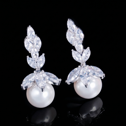 Pair of elegant drop earrings featuring shimmering marquise-cut cubic zirconia arranged in a botanical leaf silhouette with a round white faux pearl hanging at the bottom, isolated on a reflective black background.