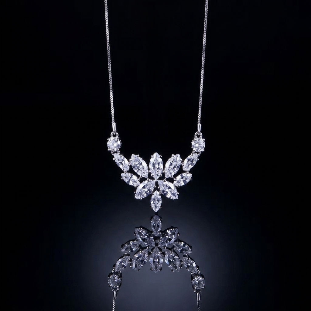 A detailed close-up product photograph of a delicate white-metal chain necklace hanging against a deep black, reflective background. The focus is on the central pendant, a sophisticated cluster of brilliant and marquise-cut shimmering stones carefully arranged into a symmetrical, multi-layered lotus or crown pattern. A partial, softened mirror reflection is visible directly beneath the pendant, enhancing its intricate sparkle. The chain is fine and unadorned.