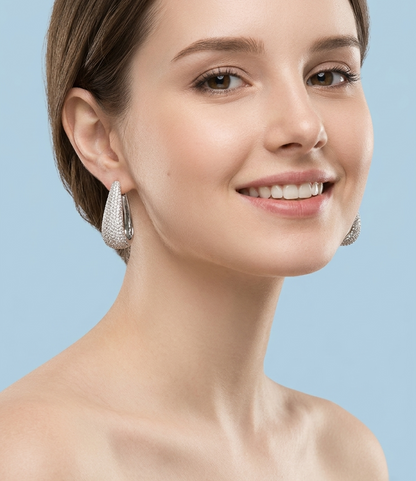 Close-up portrait of a woman wearing elegant, pavé-set silver teardrop hoop earrings, reflecting a minimalist and sophisticated jewelry style.