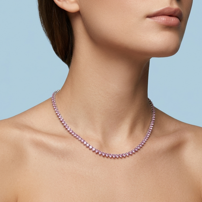 Close-up portrait of a female model wearing a sparkling pink stone tennis necklace, styled with bare shoulders to highlight the elegant design against a solid light blue background, professional jewelry campaign photography.